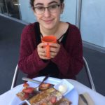 Zoe smiles at the camera, holding an orange mug.